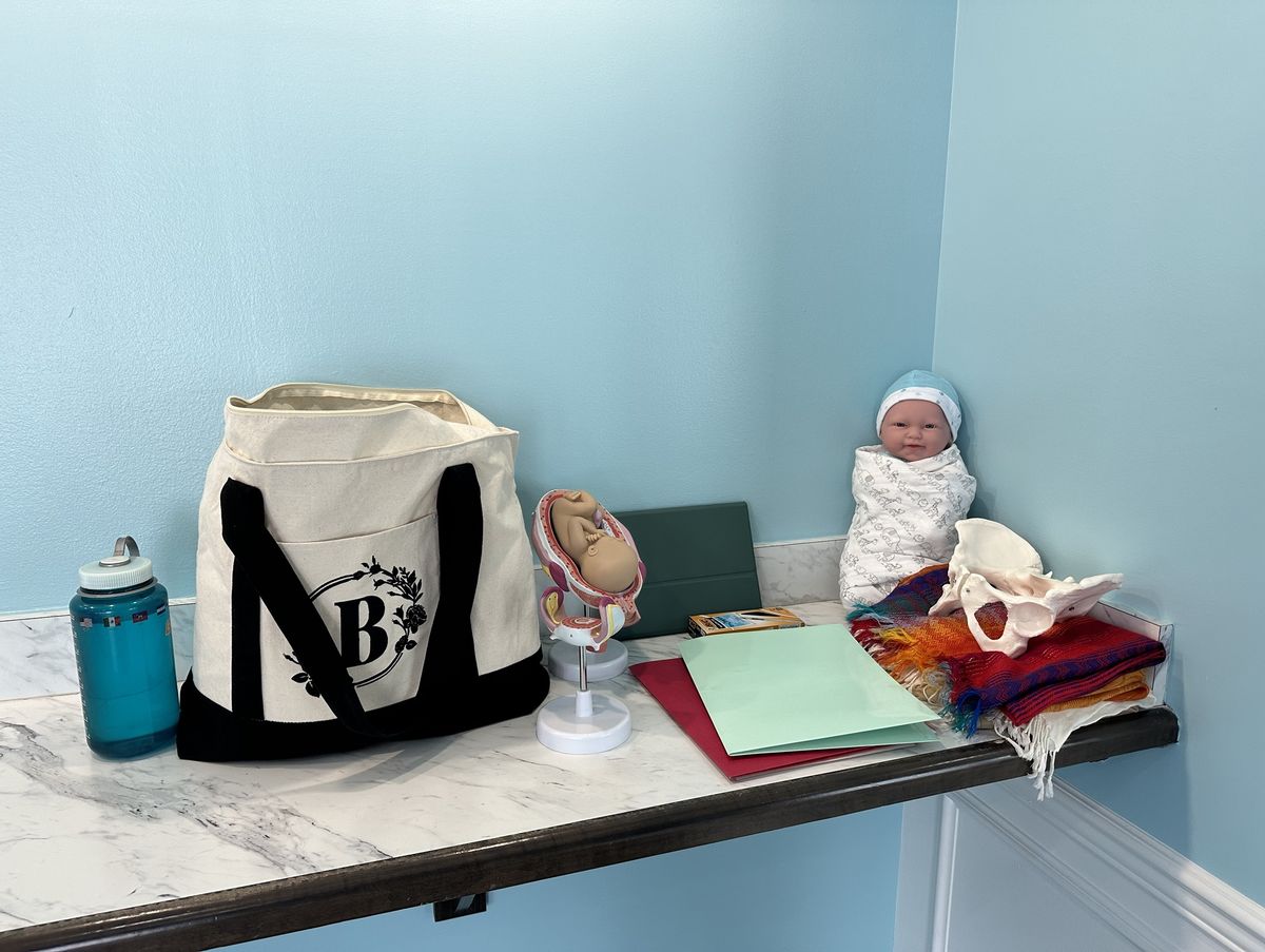 Childbirth class teaching tools: a pelvis model, a fetal model, a newborn doll, rebozo wraps, and handouts