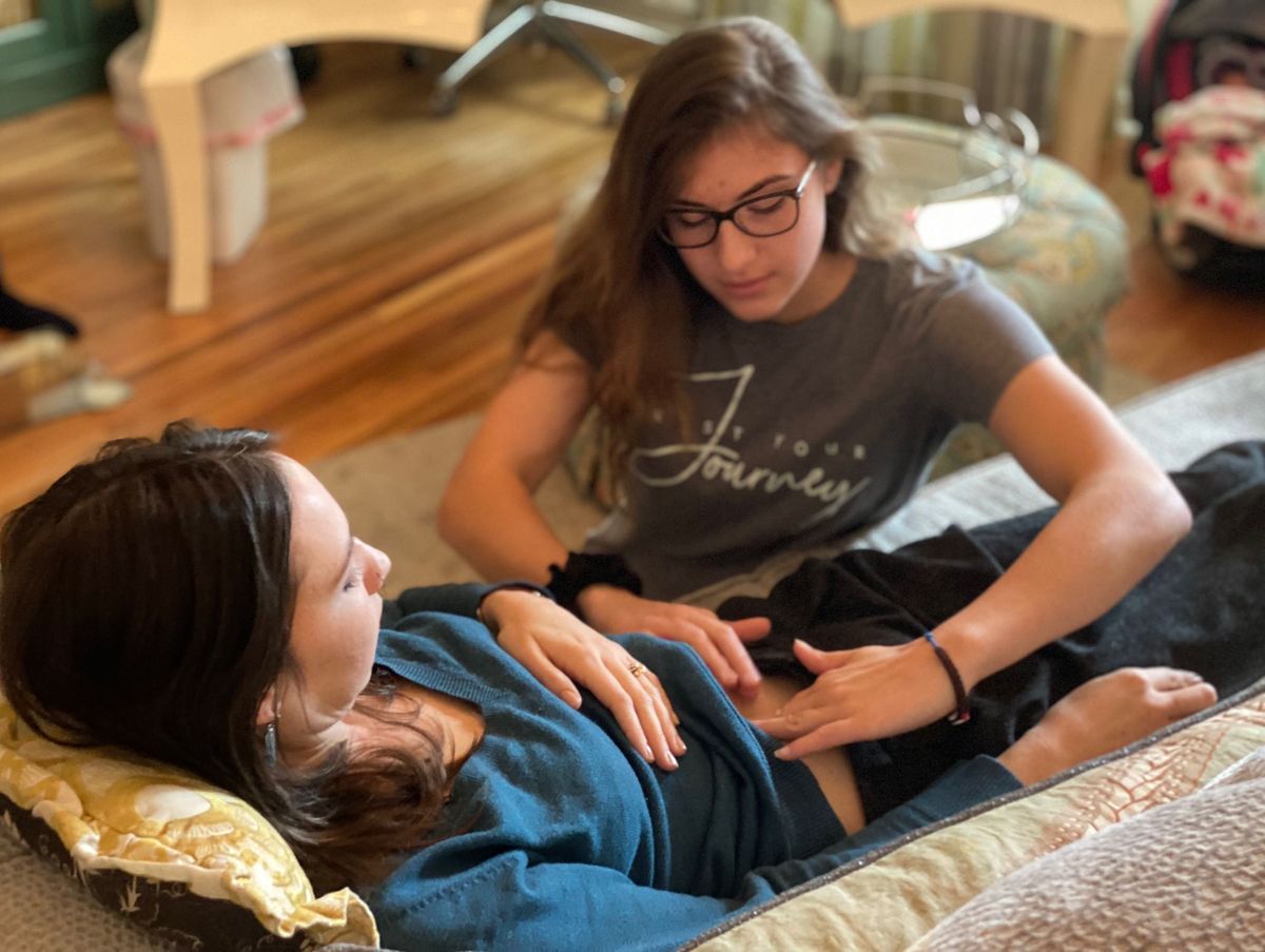 Taylor gently feels a pregnant mother's belly during a prenatal visit at home